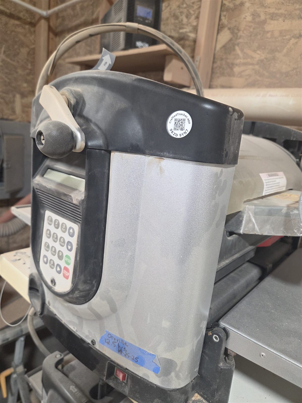 A round QR label stuck on the black top housing of a thickness planer, above the depth-stop crank and the control keypad